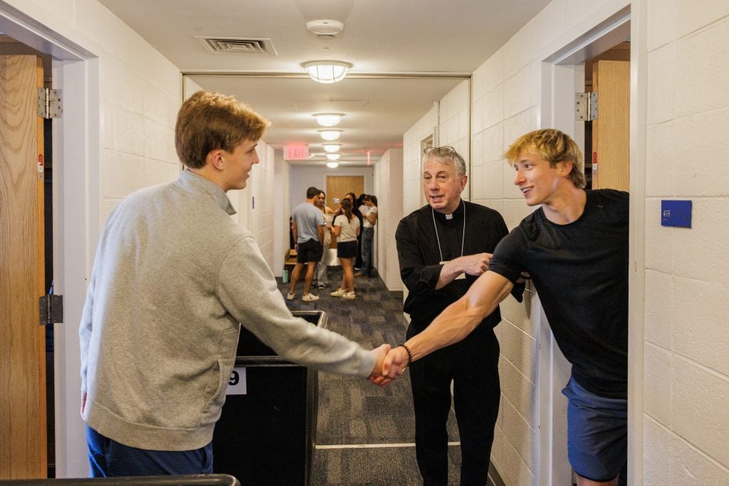 Two men shake hands in a dorm hallway