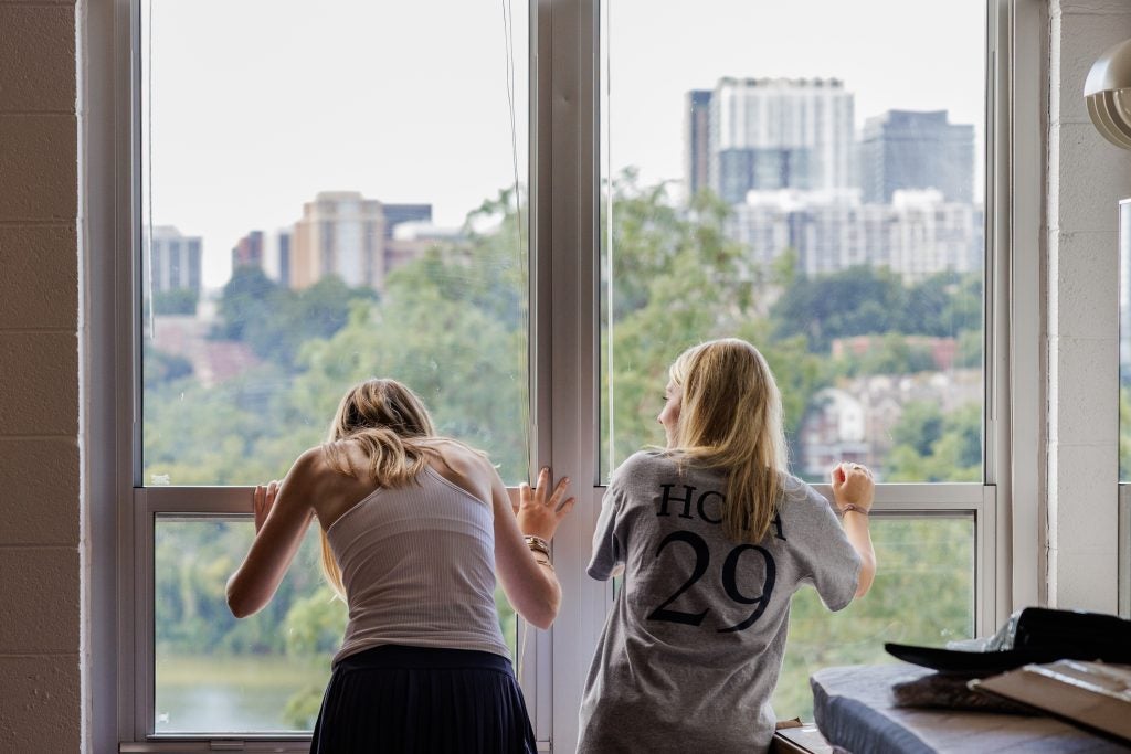 Two students stare out their dorm room window at skyscrapers