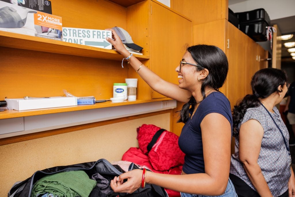 A student smiles as she places a block sign that says "Stress Free Zone" on a shelf in her dorm room