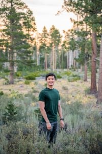 Bennie in a green shirt standing in some foliage during sunset with woods behind him.