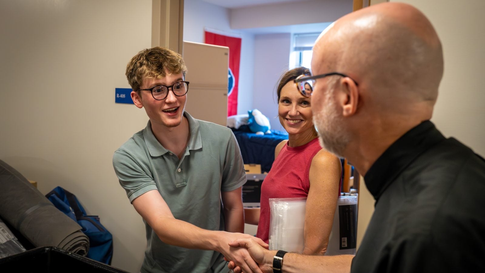 Fr Downing shakes hands with a student moving into his dorm while his mother watches