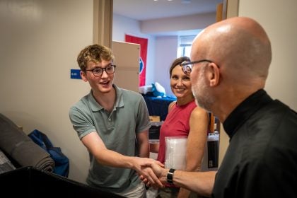 Fr Downing shakes hands with a student moving into his dorm while his mother watches