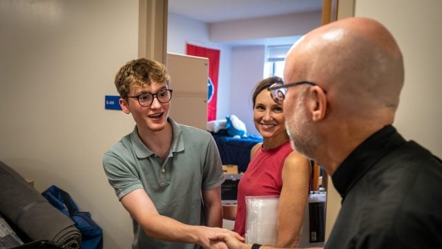 Fr Downing shakes hands with a student moving into his dorm while his mother watches