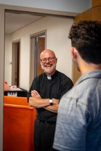 Fr Downing with arms crossed and smiling while taking with a student