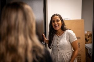 Janaki in a white dress greets someone at her apartment door