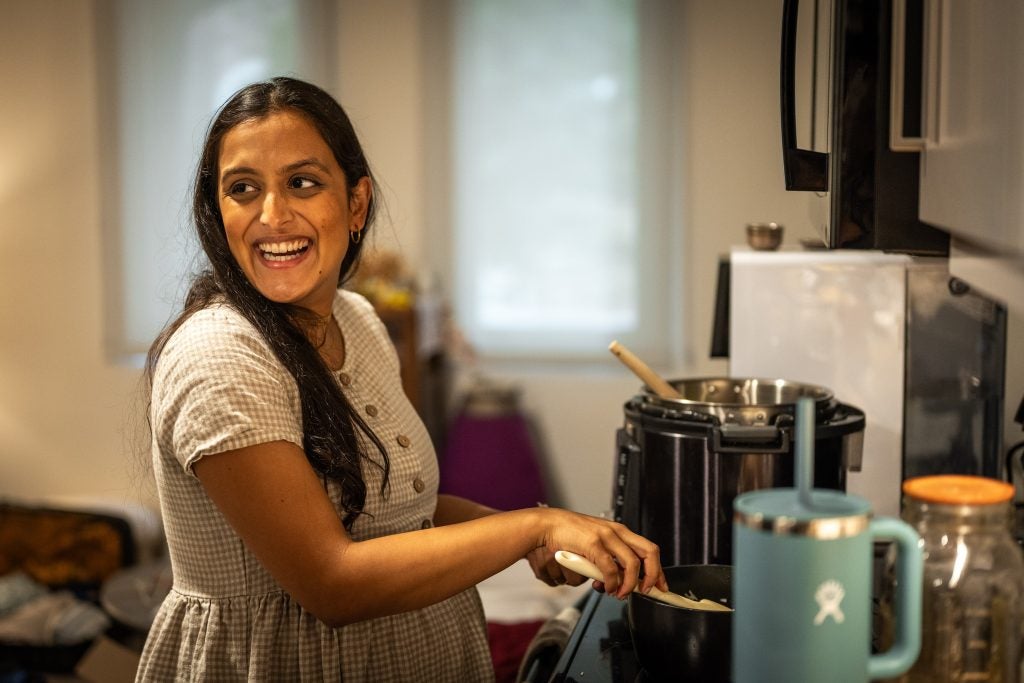 A woman smiles while stirring a pot on the stove
