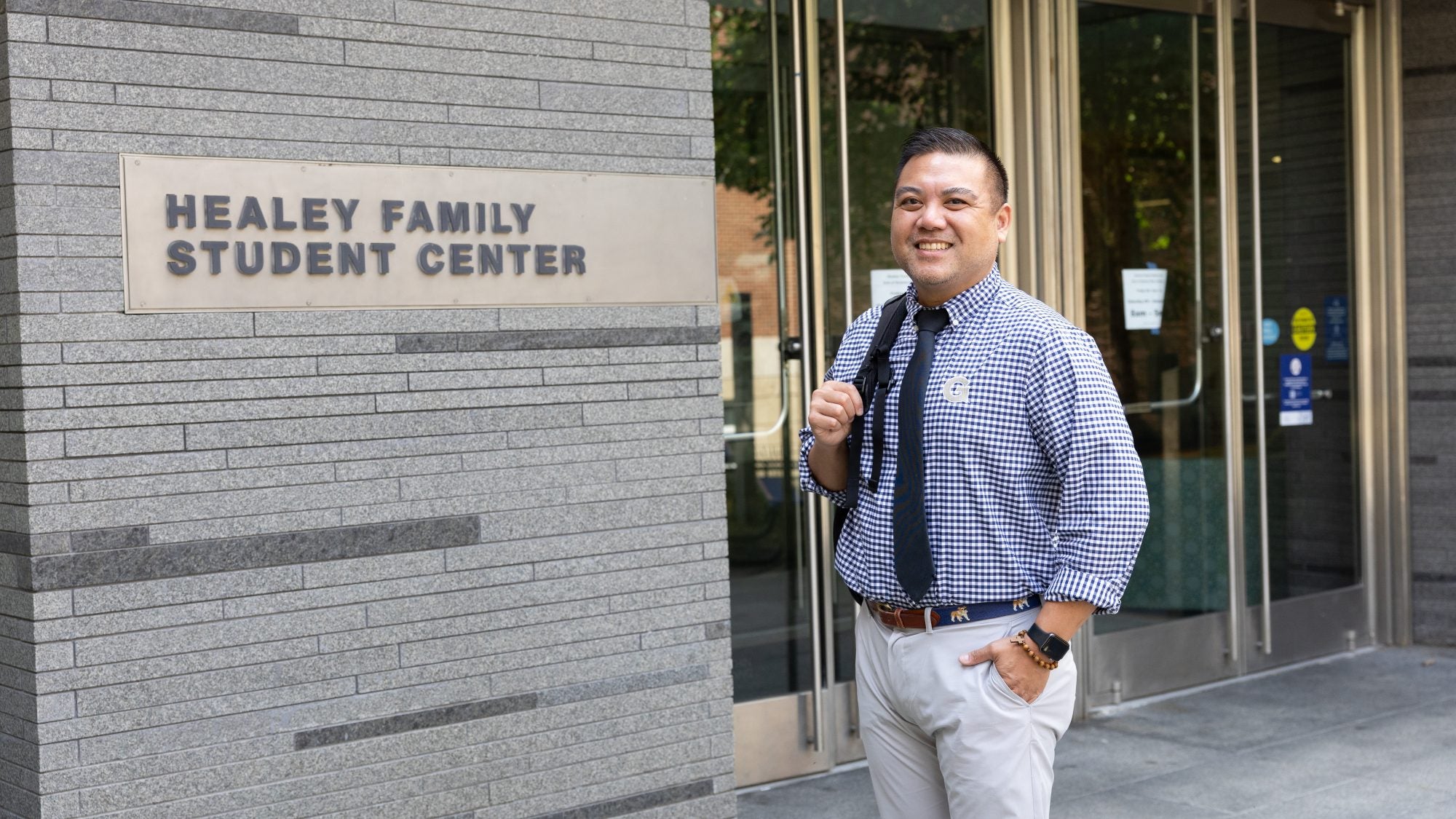 Patrick in a blue shirt and tie with a backpack over his shoulder in front of HFSC