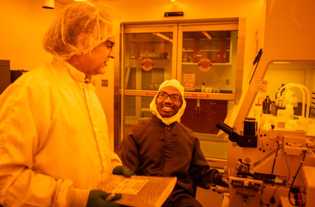 Paranjape speaks to his student in a yellow lit lab