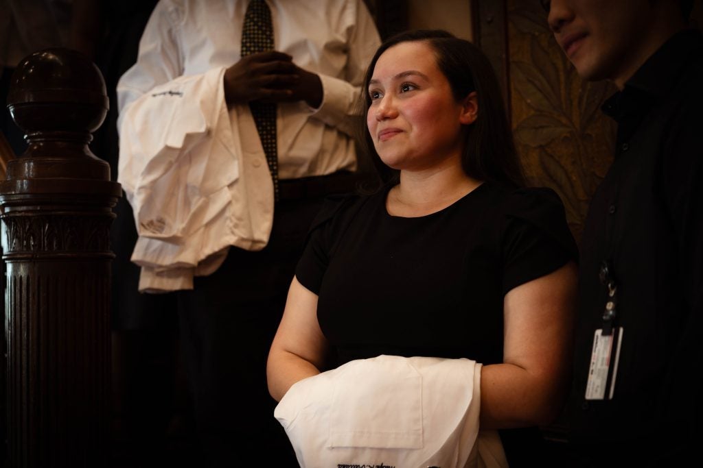 A young woman in a black shirt holds a white coat and smiles