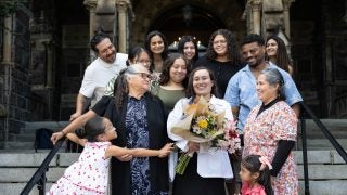 A family gathers around a student wearing a white coat and holding flowers on stone steps