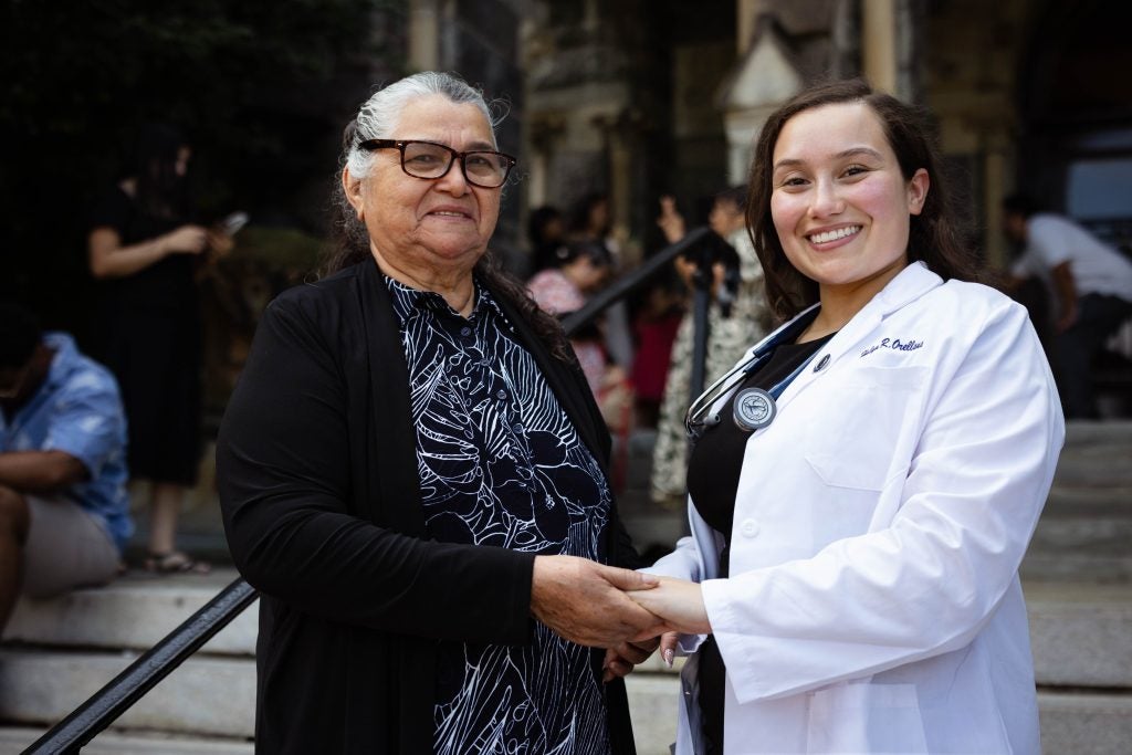 A grandmother and her granddaughter smile and pose together on stone steps