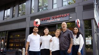 A group of students and owners of a bakery stand in front of a Good Company Doughnut & Coffee cafe