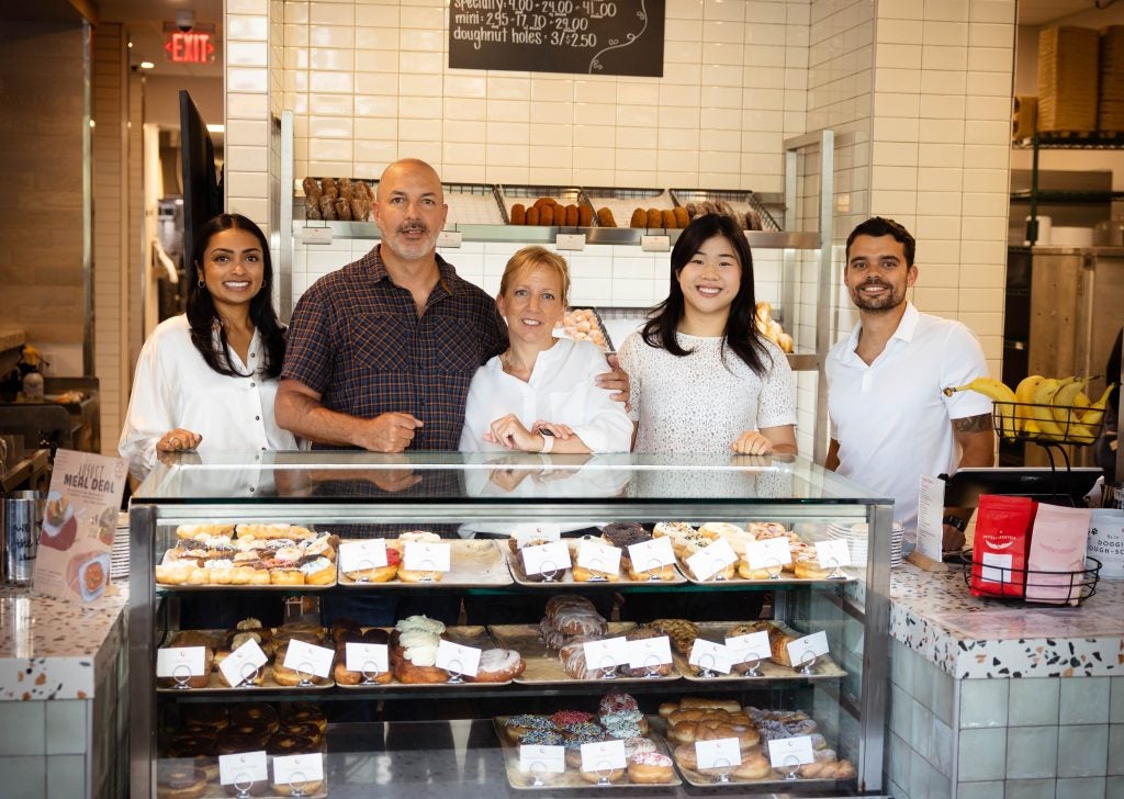 A group of people stand behind a donut case in a bakery