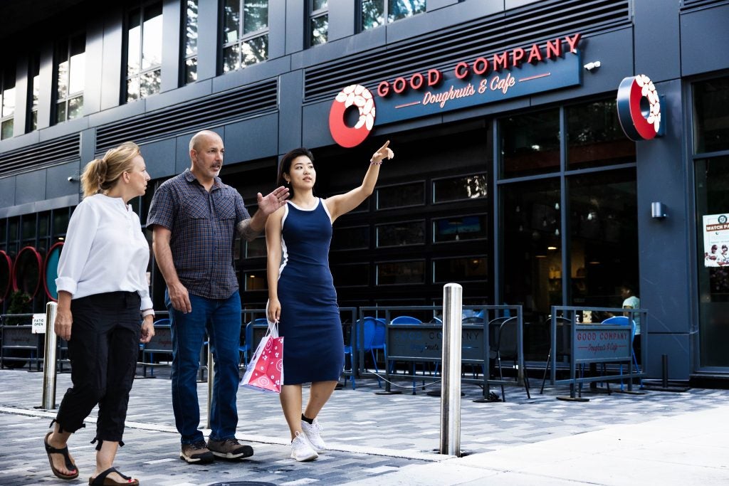 A woman points to two others as they walk in front of a donut shop