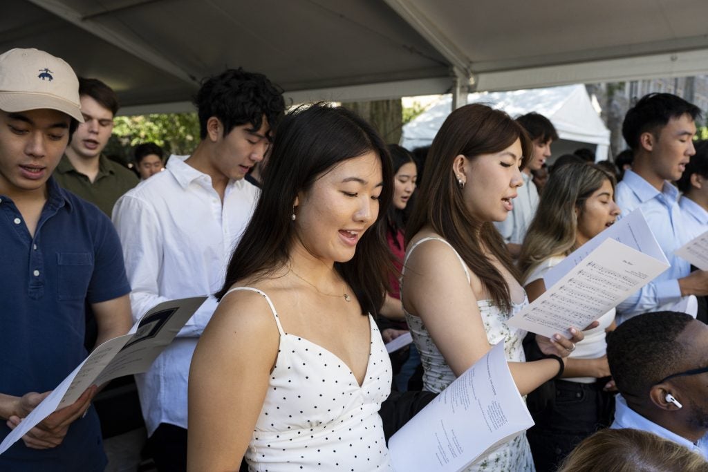 A group of students sing while looking at a booklet