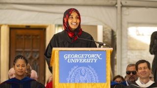 A student wearing a hijab smiles during her speech behind a podium