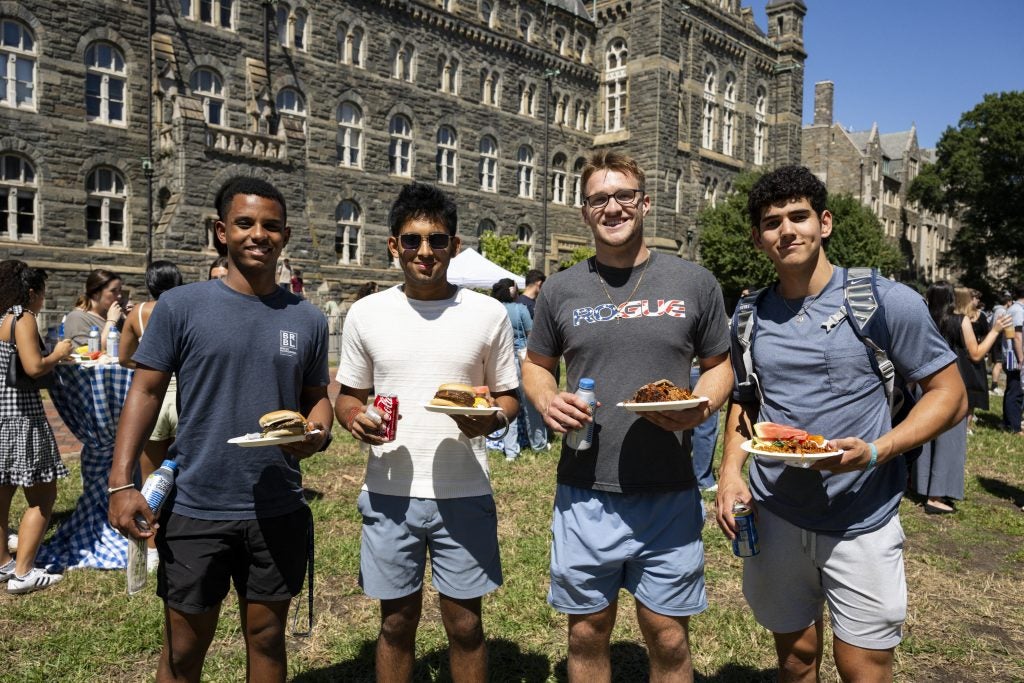 A group of male students smile while holding plates at a BBQ