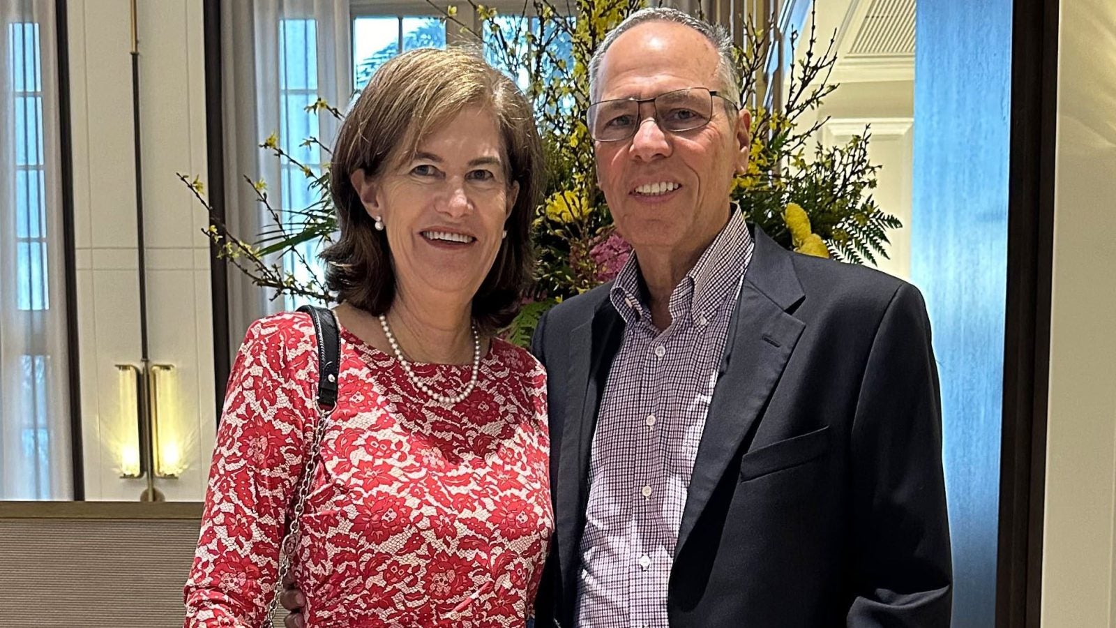 A woman in a red patterned dress poses with her husband in a black suit and purple button-up shirt