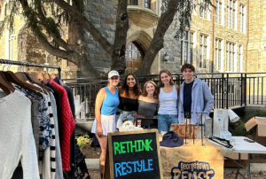 Four students pose with a sign that says "REUSE" and a clothing rack.
