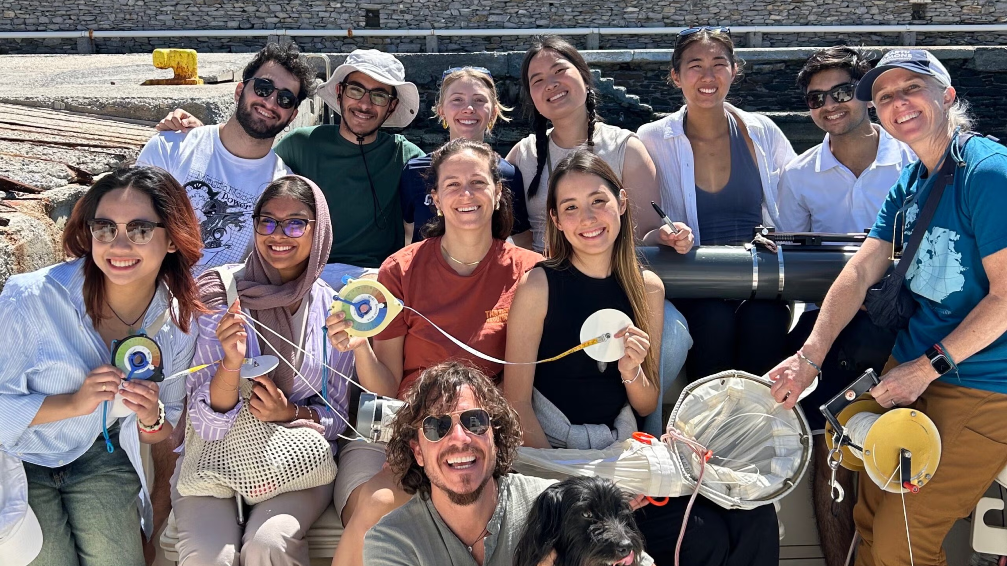 A group of students smile on a boat with a dog
