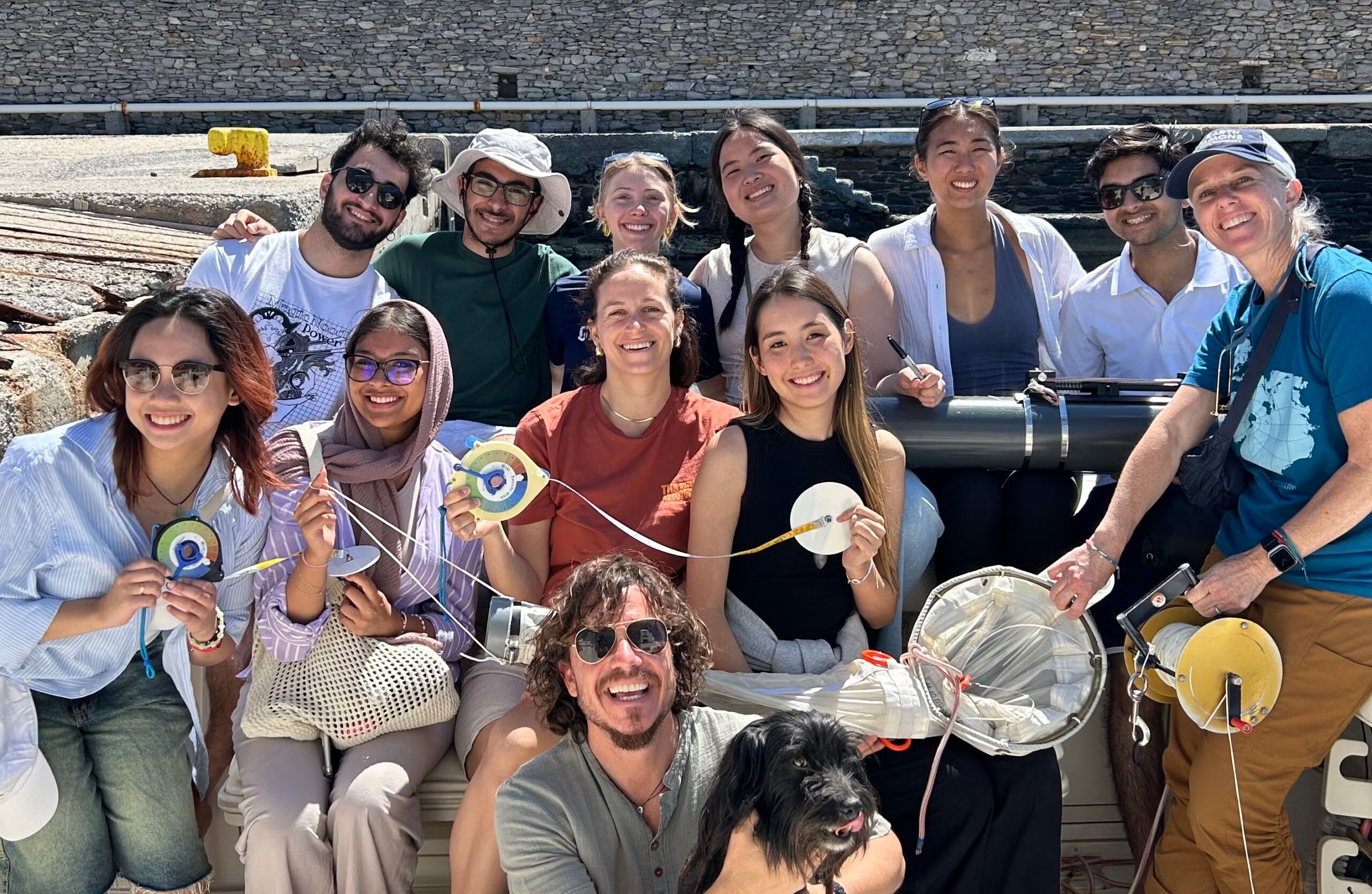 A group of students smile on a boat with a dog