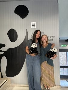 Two students hold panda bears in front of a painting of a panda bear at World Wildlife Fund in Greece