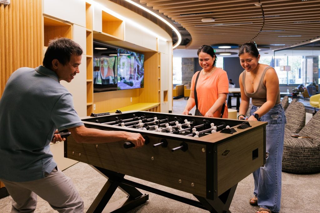 Three young people play foosball in a common area