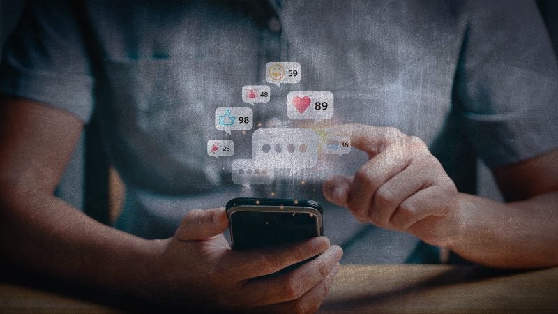 A man taps a phone as graphics of social media come appear above it