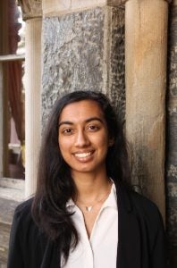 A female student smiles in front of a stone wall.