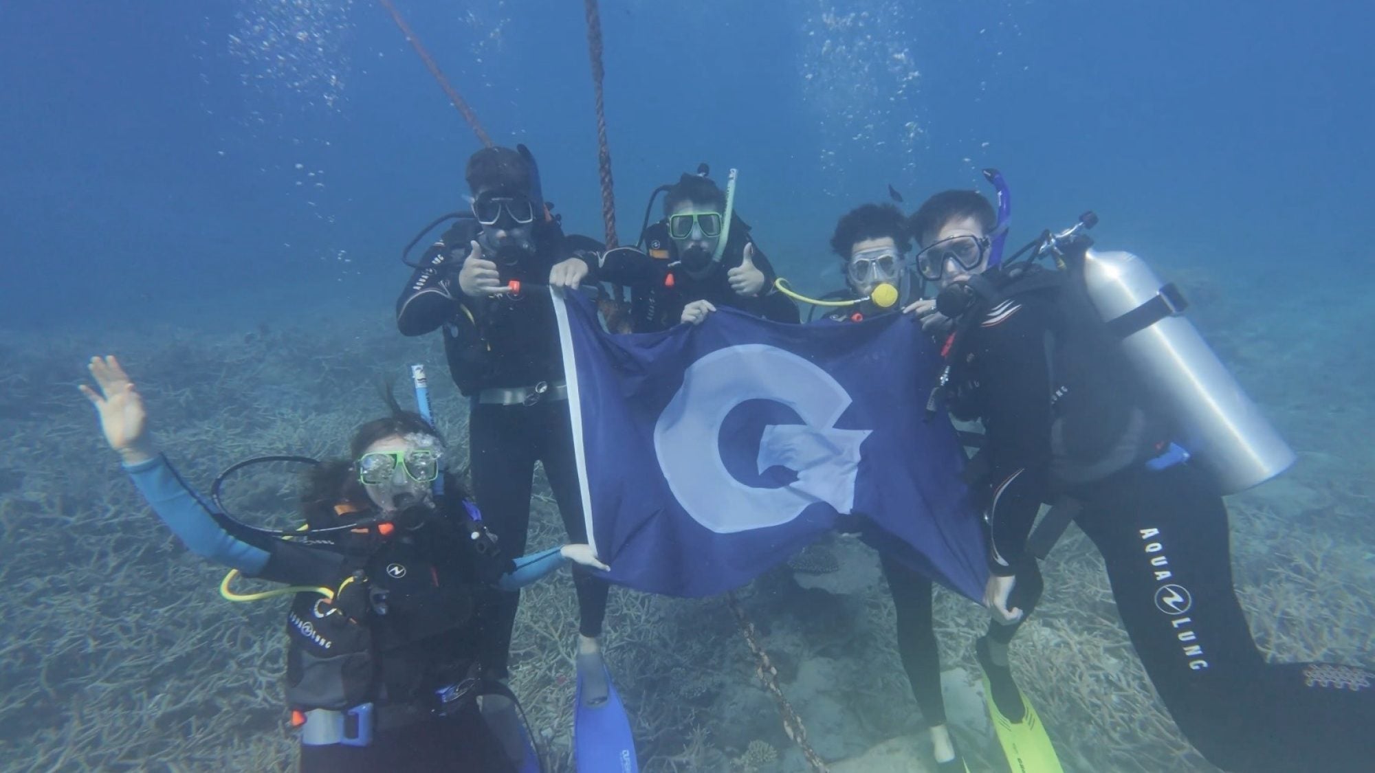 GU students underwater in diving gear holding a GU flag