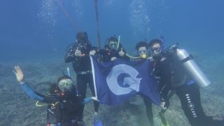 GU students underwater in diving gear holding a GU flag