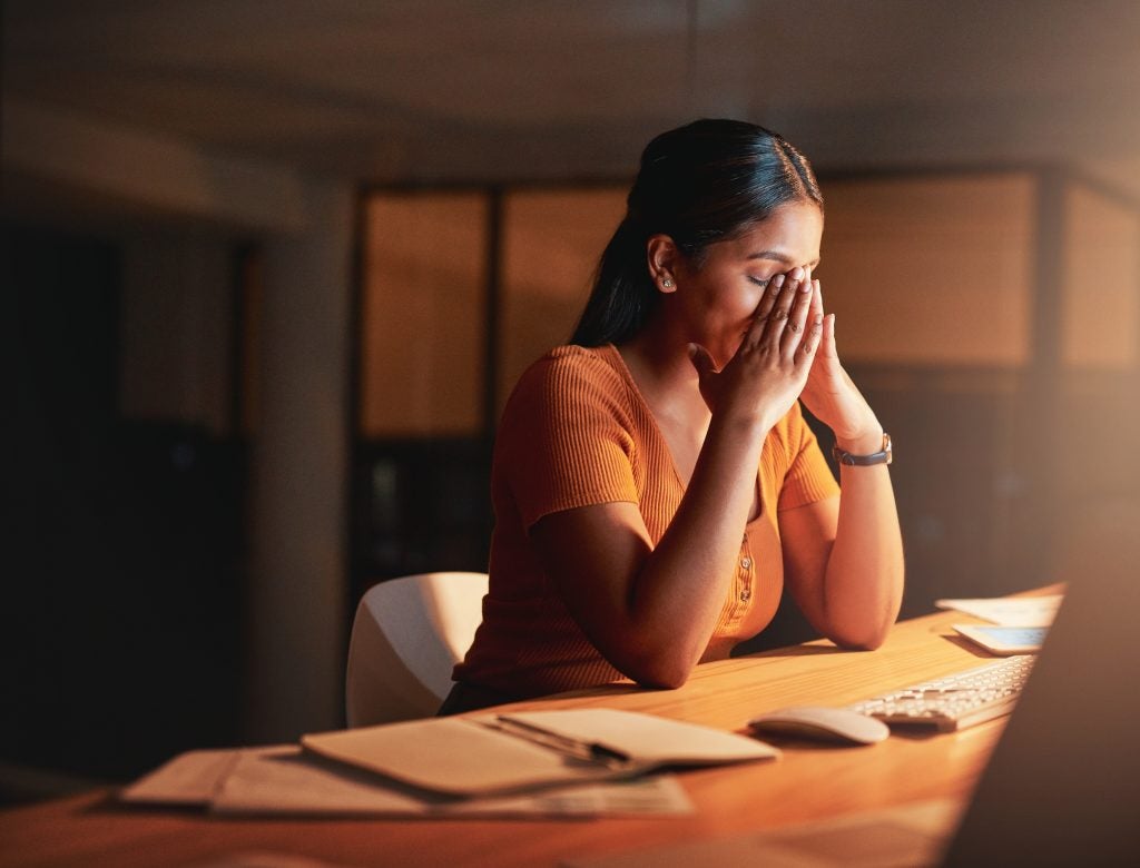 Shot of a young businesswoman sitting alone in the office at night and feeling stressed