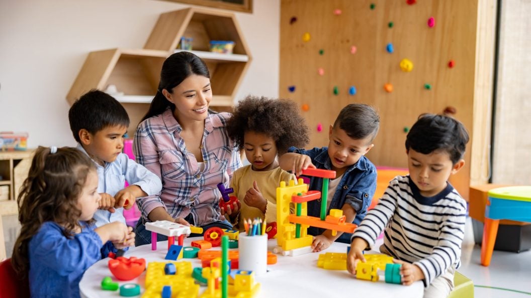 Young female child care worker with five young children at a play table