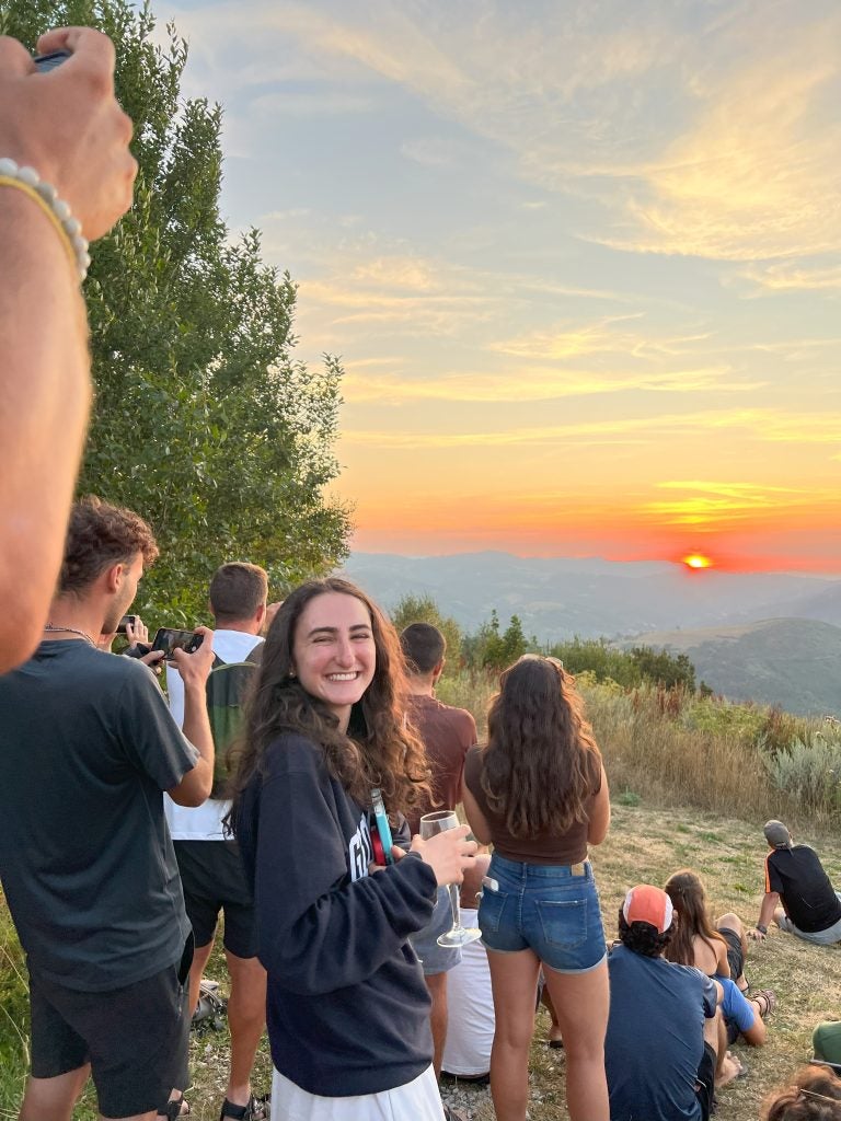 Young woman looks back at the camera while sun sets over a mountain on a clear day