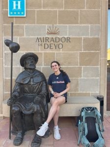 Young woman in blue shift next to a sculpture of a man in Spain
