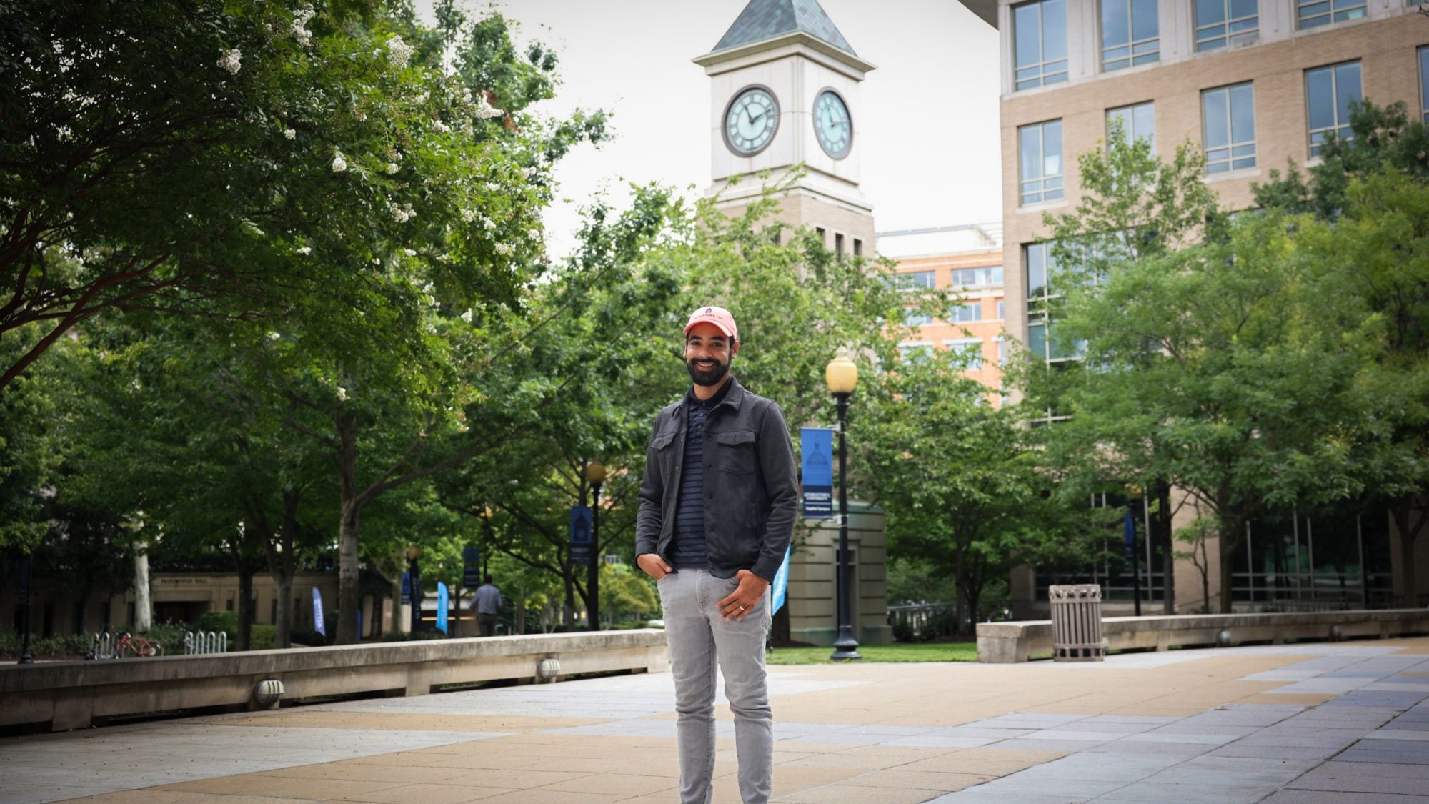 A man wearing an orange baseball cap stands in front of a clocktower
