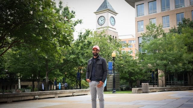A man wearing an orange baseball cap stands in front of a clocktower