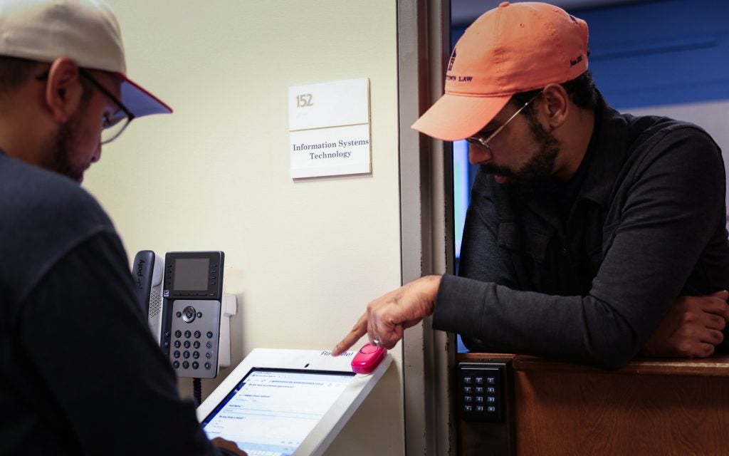 A man in an orange baseball cap helps someone fill out an online form