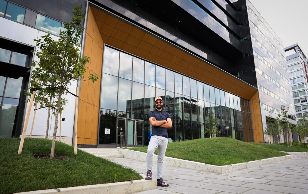 A man in an orange cap stands in front of a glass-walled building
