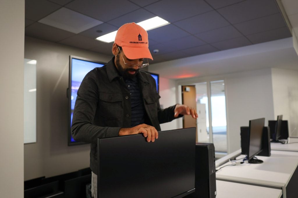 A man in an orange baseball cap installs a laptop in a classroom