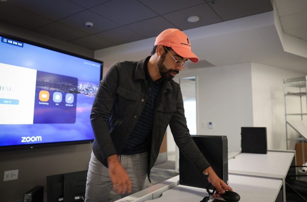 A man in an orange cap installs technology in front of a screen in a classroom