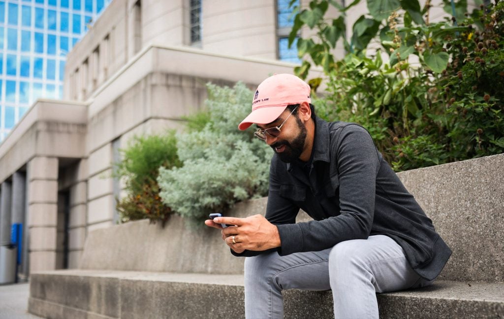 A man in an orange baseball cap looks at his phone on steps outdoors
