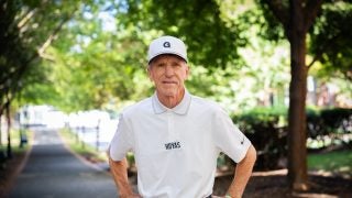 Older Caucasian man in a white hat and GU shirt with hands on hips