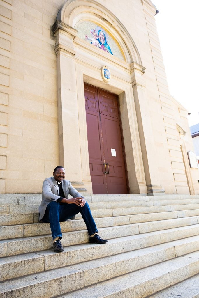 A man wearing a clerical collar sits on the steps of a church
