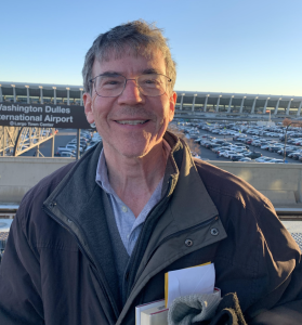Older white man with glasses in a jacket at Dulles airport