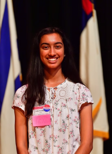 A student wears a nametag and smiles in front of a flag