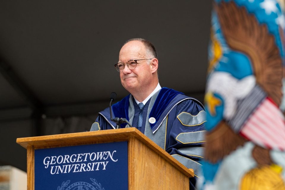 President DeGioia smiles from behind a podium wearing an academic robe