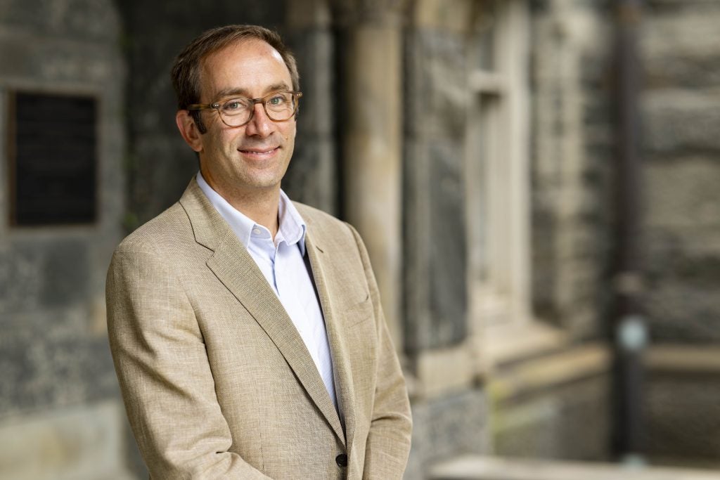 A male professor wearing glasses and a blazer smiles
