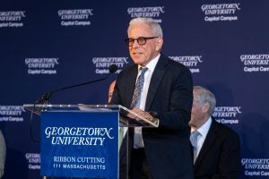 Caucasian man in a suit with glasses speaks at a GU podium