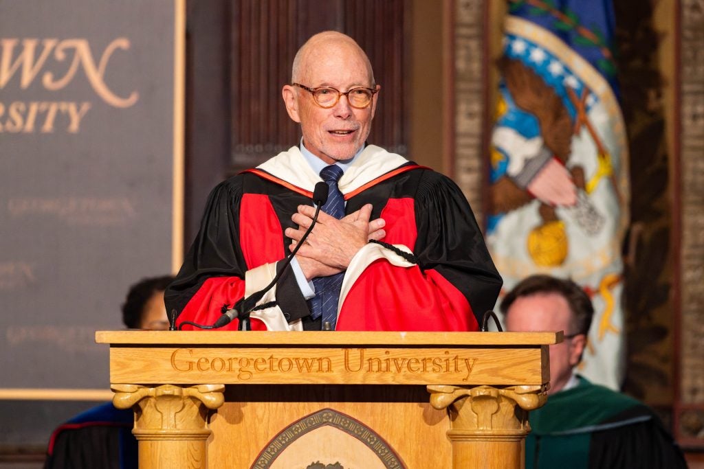 A man clutches his heard while speaking behind a podium